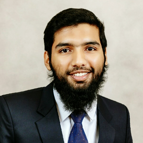 a young man with a beard wearing a suit and tie looks straight into the camera