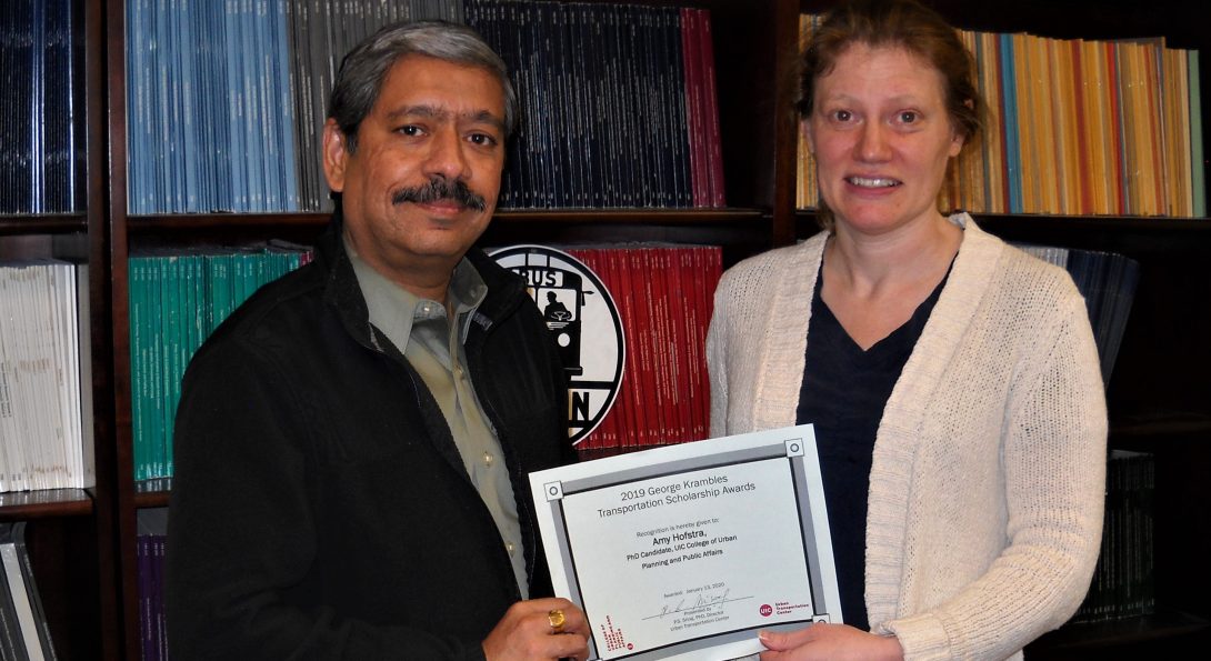 a man and woman stand next to each other in front of a bookcase, holding a certificate between them